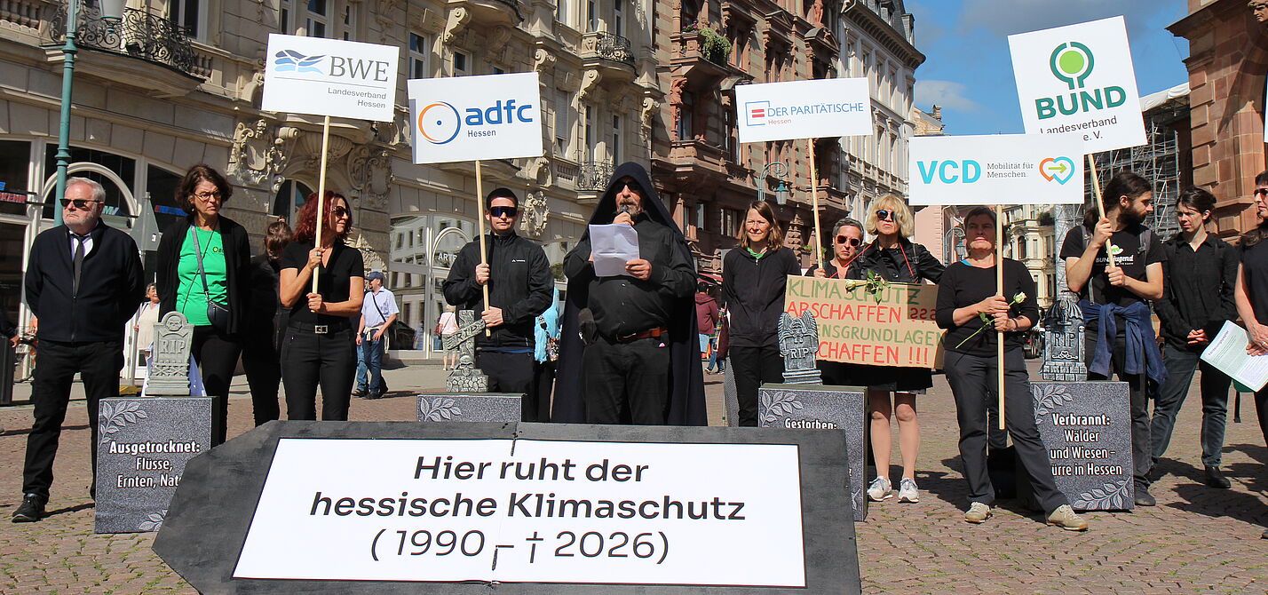 Menschen mit Schildern und Transparenten hinter einem Sarg, der die Aufschrift "Hier ruht der hessische Klimaschutz" trägt.