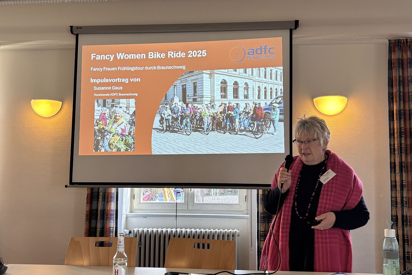Eine Frau, Susanne Gaus, steht vor einer Leinwand. Mit dem Beamer werden dort eine Grafik zum Fancy Woman Ride in Brauschweig angezeigt
