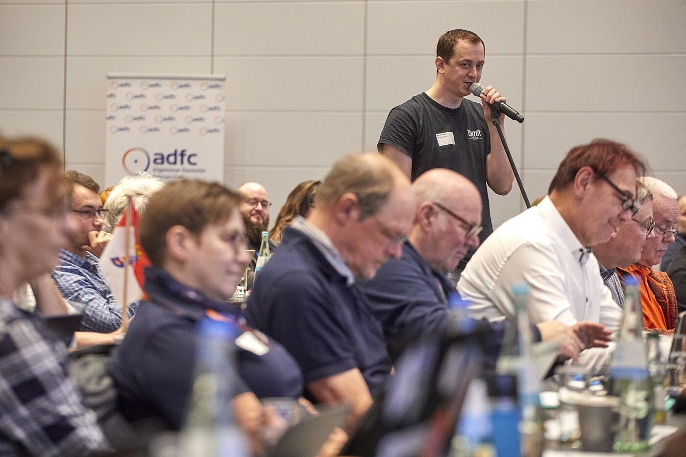 45. ADFC-Bundeshauptversammlung 2025 Ein Teilnehmer der BHV steht mit Mikrofon im Saal und spricht, während andere am Tisch sitzen und zuhören.